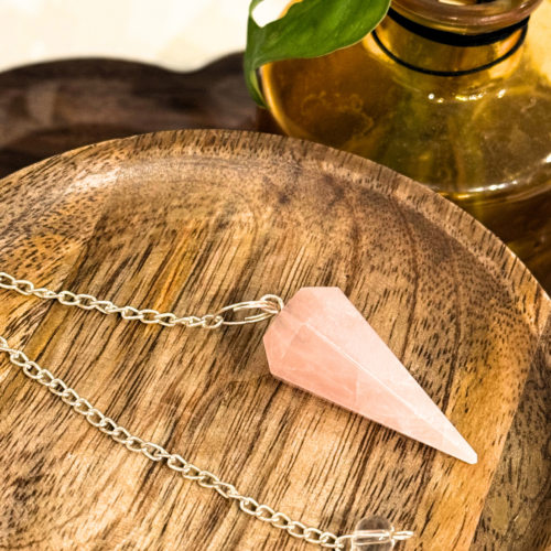 Home 2026 28 Pink rose quartz pendulum on cord, smooth polished bob, against bone background.