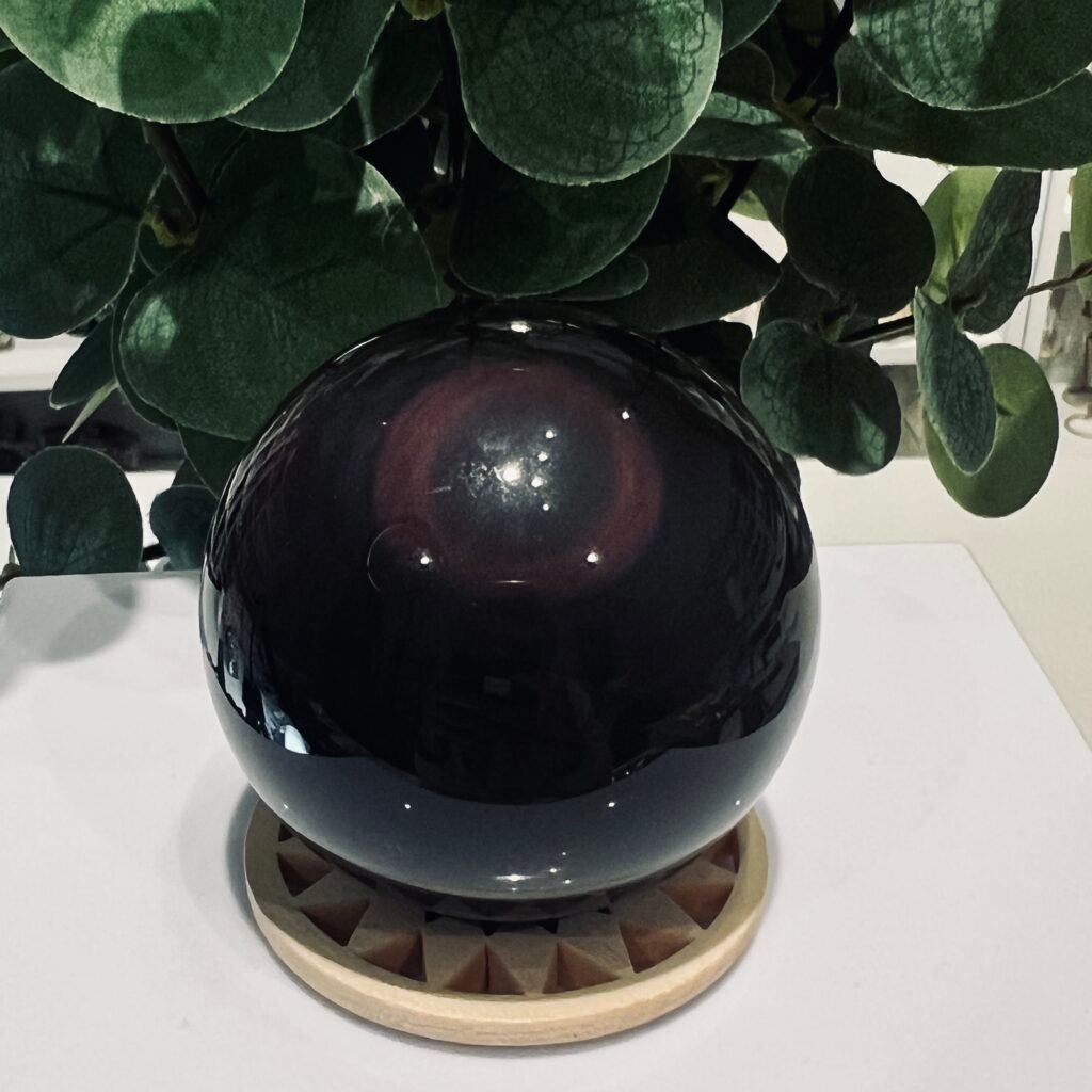 Rainbow obsidian sphere 53mm on a wooden sphere stand, polished black volcanic glass with a purple bullseye ring, Mystic Grove UK