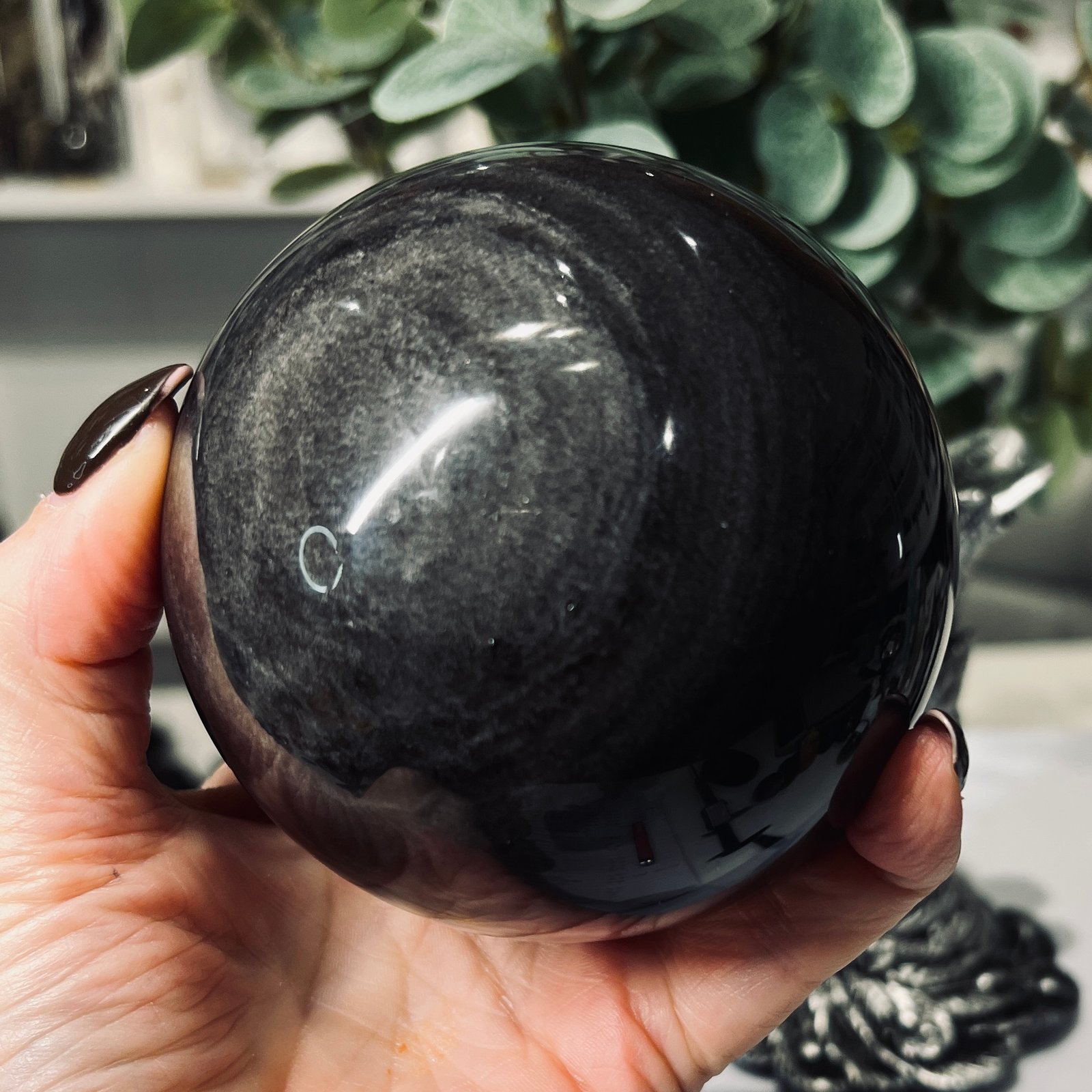 Silver Sheen Obsidian Sphere 90mm with Silver Stand 2 Silver sheen obsidian sphere held in the hand showing the silver ring pattern