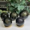 Four gold sheen obsidian spheres and one rainbow obsidian bullseye sphere on wooden stands Four gold sheen obsidian spheres and one rainbow obsidian bullseye sphere on wooden stands