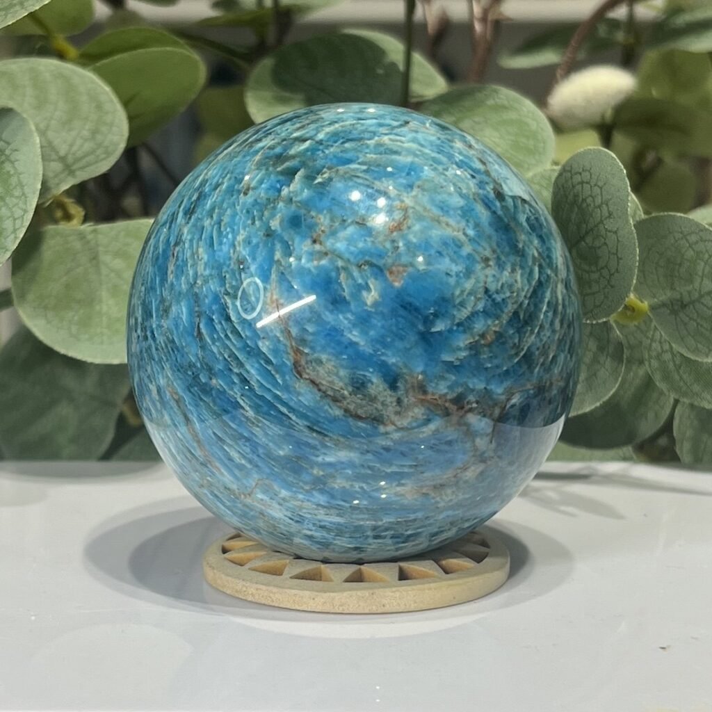 Large blue apatite sphere 72mm on a wooden stand, bright ocean blue with natural veining, Mystic Grove UK