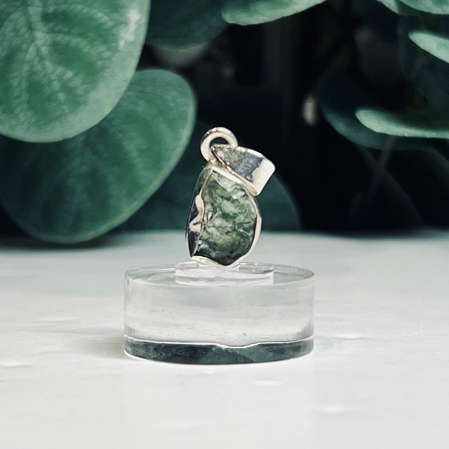 Raw moldavite pendants set in sterling silver on clear stands
